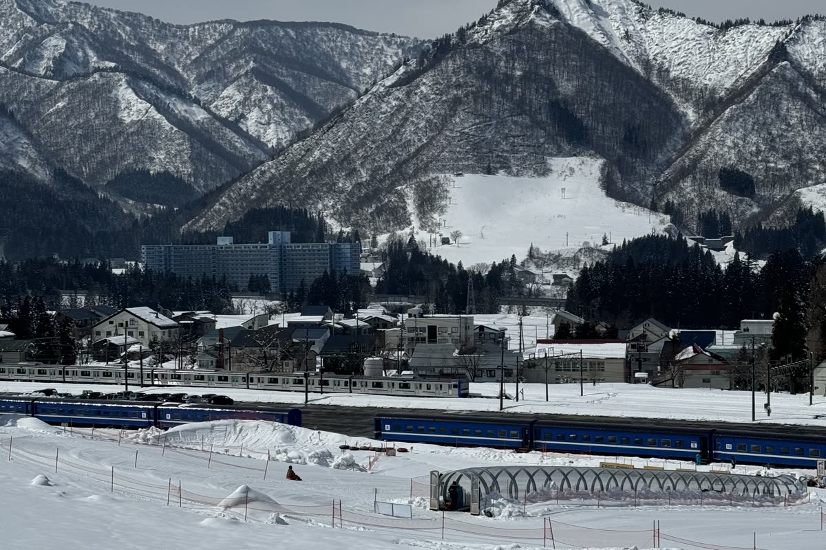 從雪場遠眺越後中里站方向,可見停靠的藍色電聯車、隧道與雪山